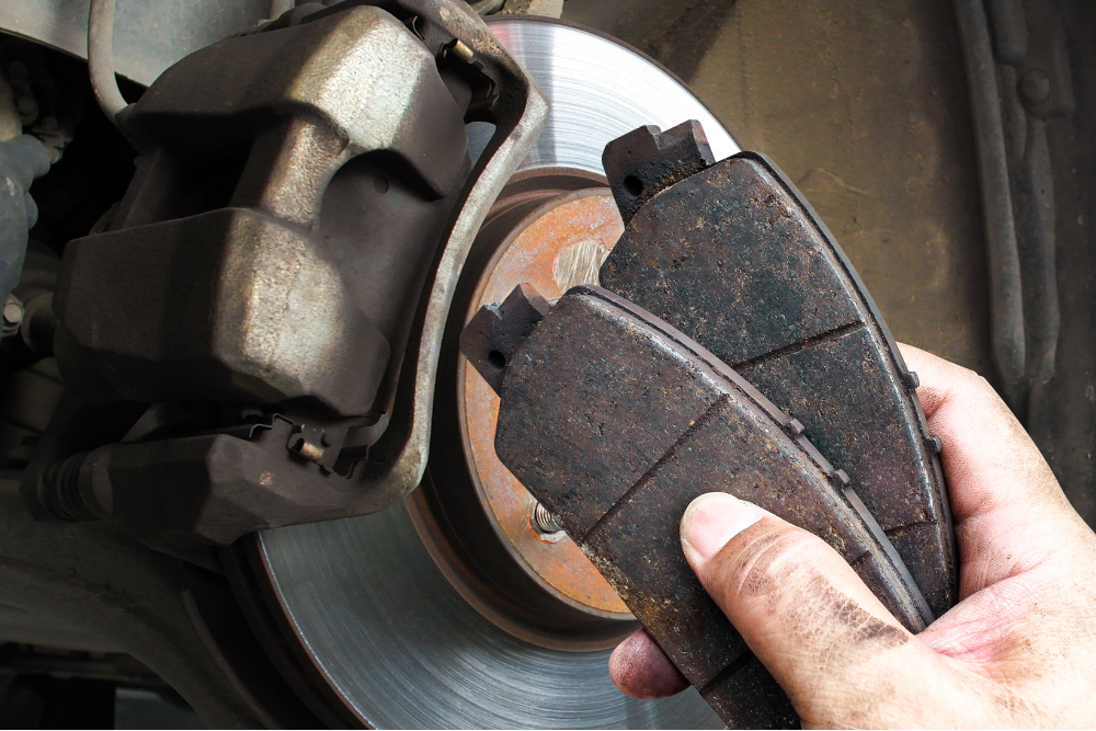 brake pads, auto repair in Buffalo, NY at Total Automotive. Brake service in progress showing a worn brake pad being compared to the rotor and caliper. The image highlights the importance of timely brake inspections to ensure vehicle safety and performance.