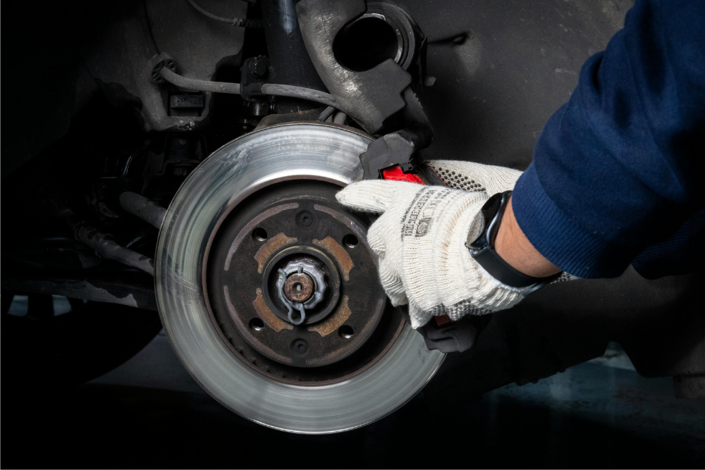 brake auto repair in Buffalo, NY at Total Automotive. Mechanic wearing gloves works on a car’s brake system, inspecting or replacing the brake caliper and disc rotor.