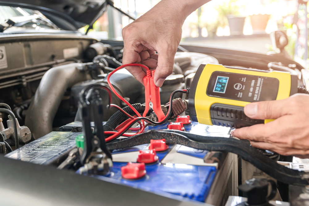 Tire & Battery Checks auto repair in Buffalo, NY at Total Automotive. Mechanic using a battery tester with red and black clamps to check a car battery’s charge under the hood.